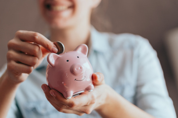 female hands hold a pink piggy bank and puts a coin there. The concept of saving money or savings, investment female hands puts a coin in a pink piggy bank. The concept of saving money or savings, investment